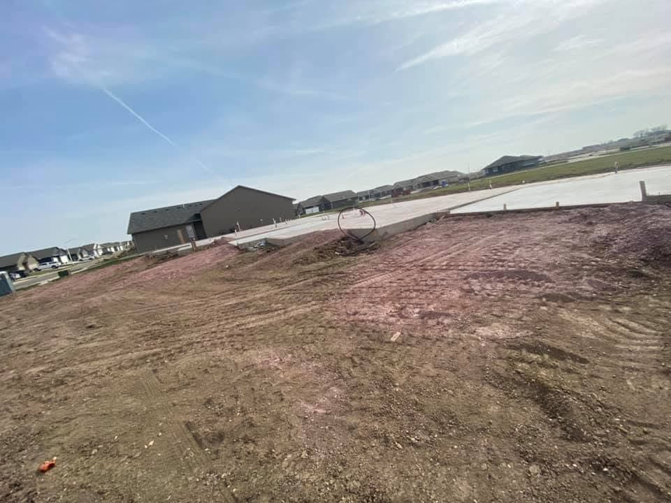 A new-construction lot with a poured slab and foundation walls in the distance
