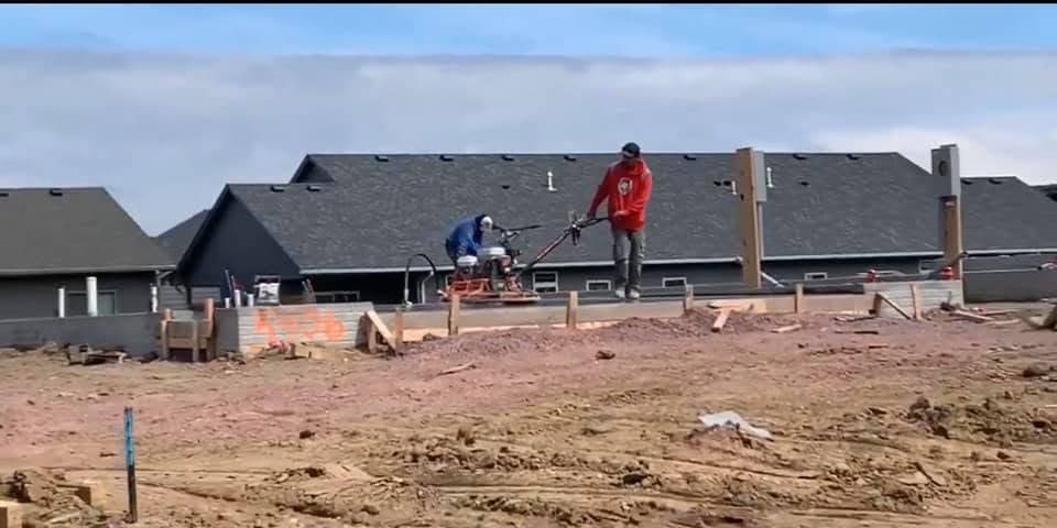 Two of our crew screeding wet concrete across a foundation as it is placed