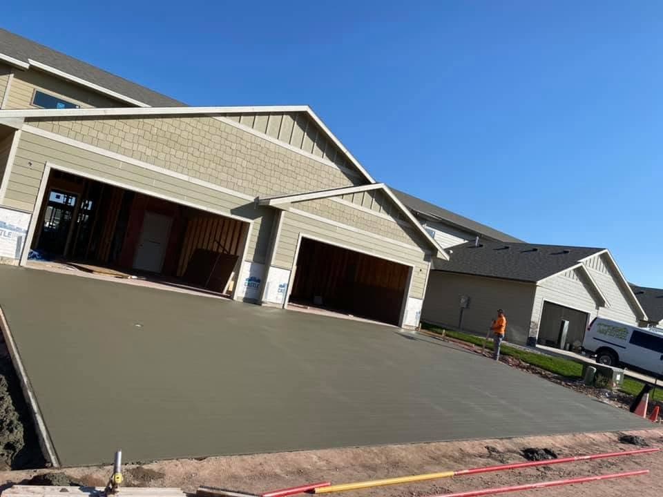 A wide concrete driveway sloping up to the garages of a craftsman-style home under construction