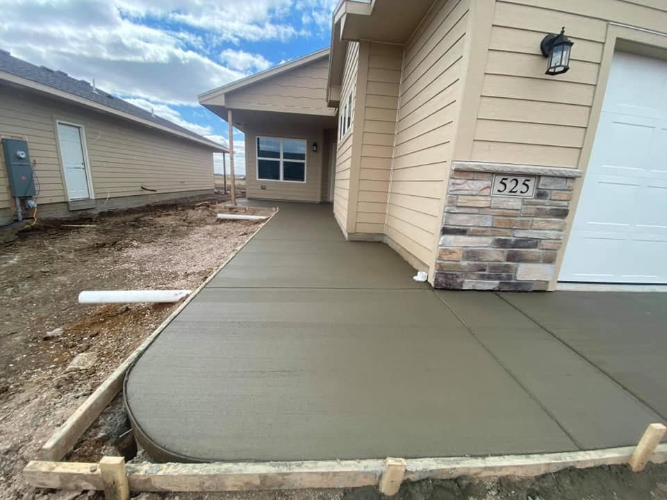 A finished concrete approach with a rounded formed edge curving past the stone-accented entry of a new home