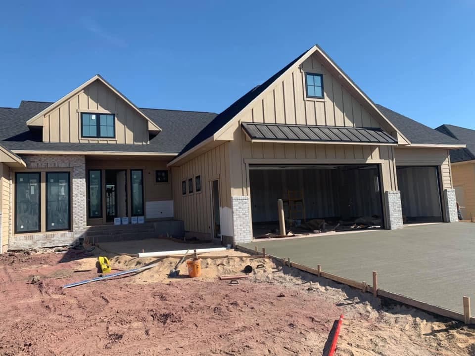 A finished concrete driveway across the front of a modern farmhouse with a three-stall garage
