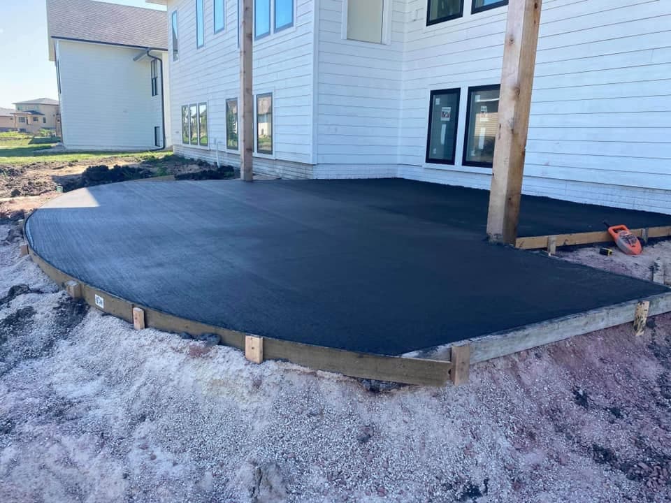 A finished backyard patio slab with a rounded formed edge against a new home