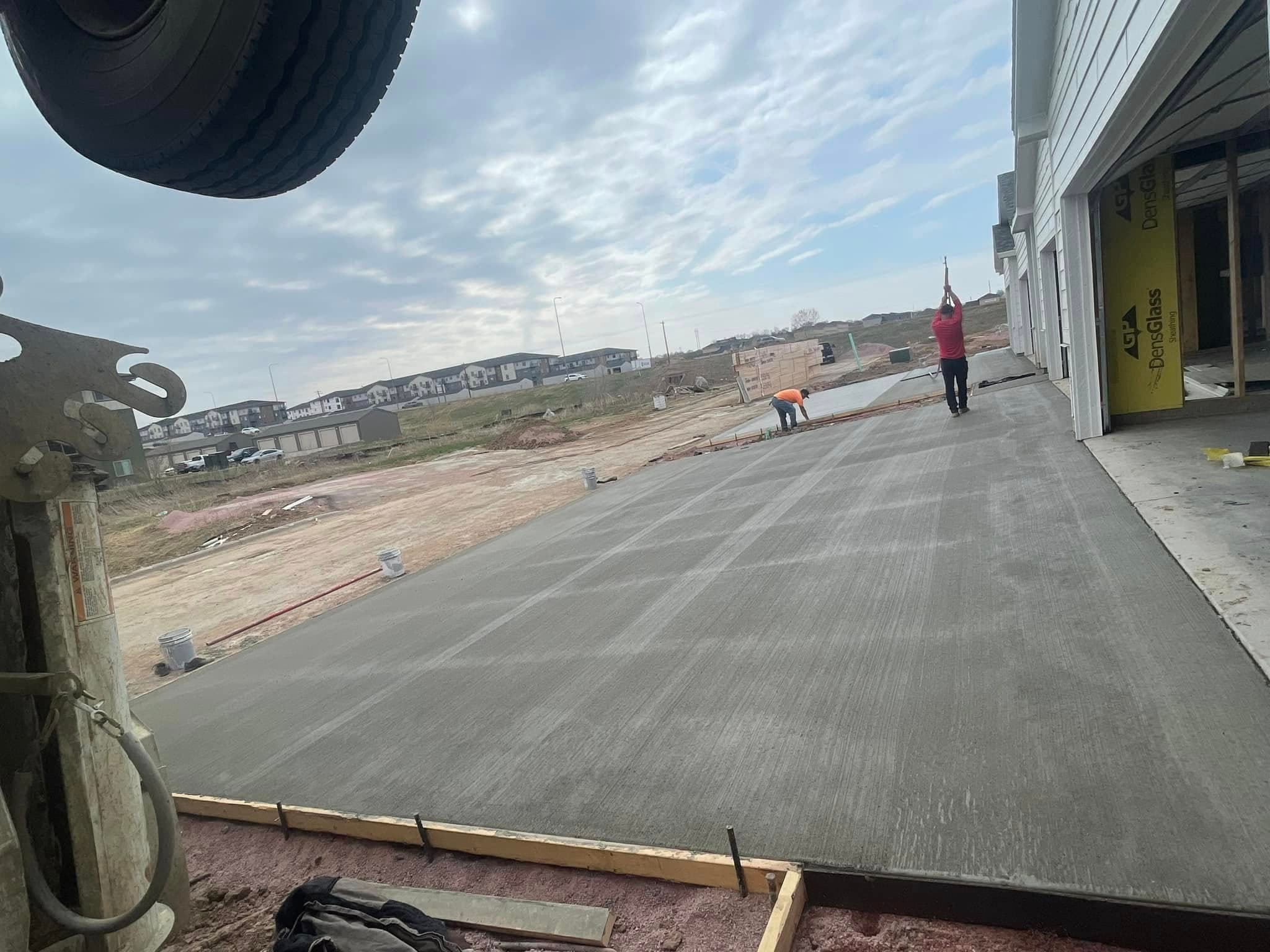 A wide concrete apron finished out from a new garage as our crew works the far edge, seen from the pump truck