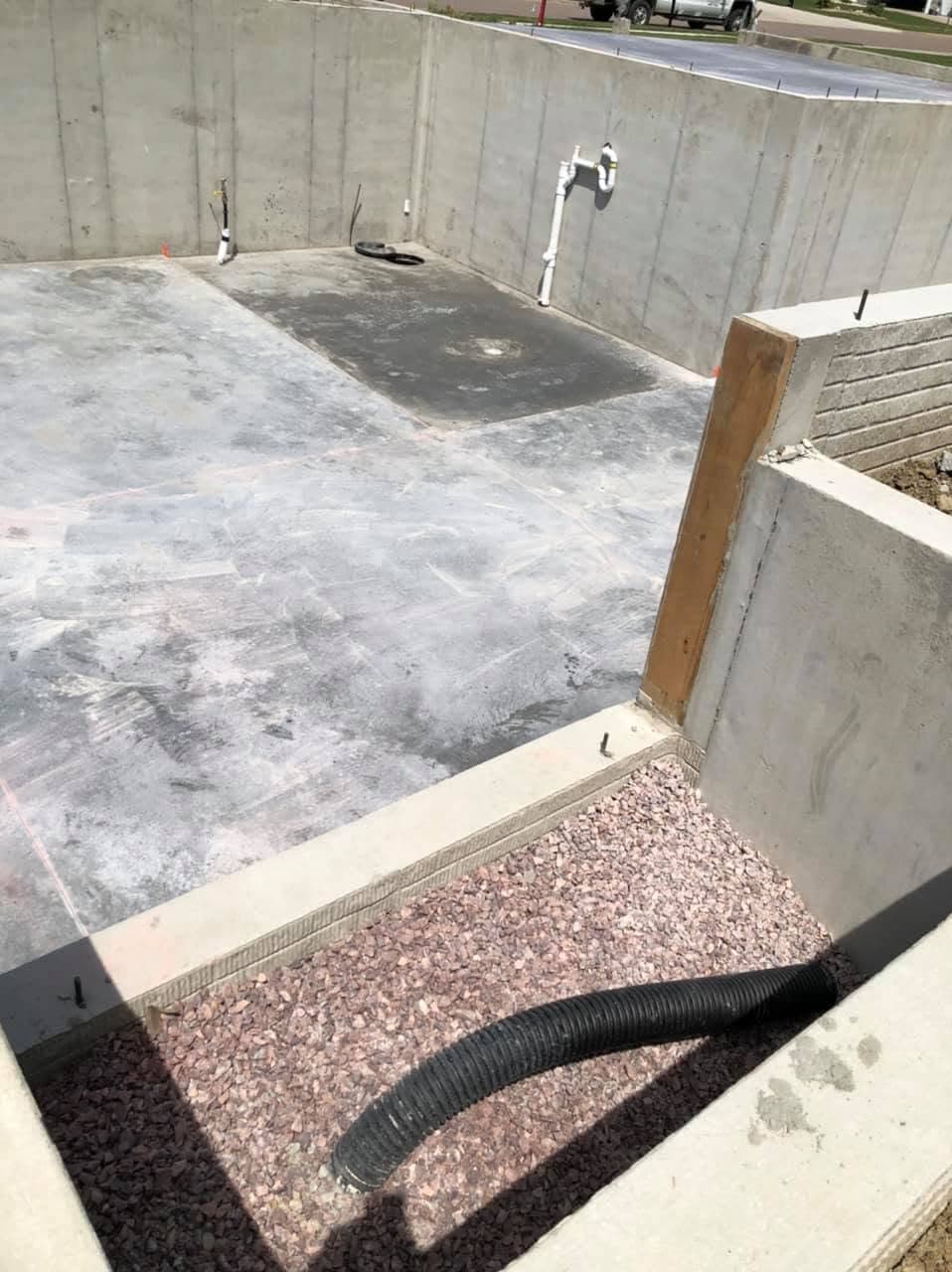 A finished basement floor slab poured inside concrete foundation walls, with plumbing stub-ups and a floor drain
