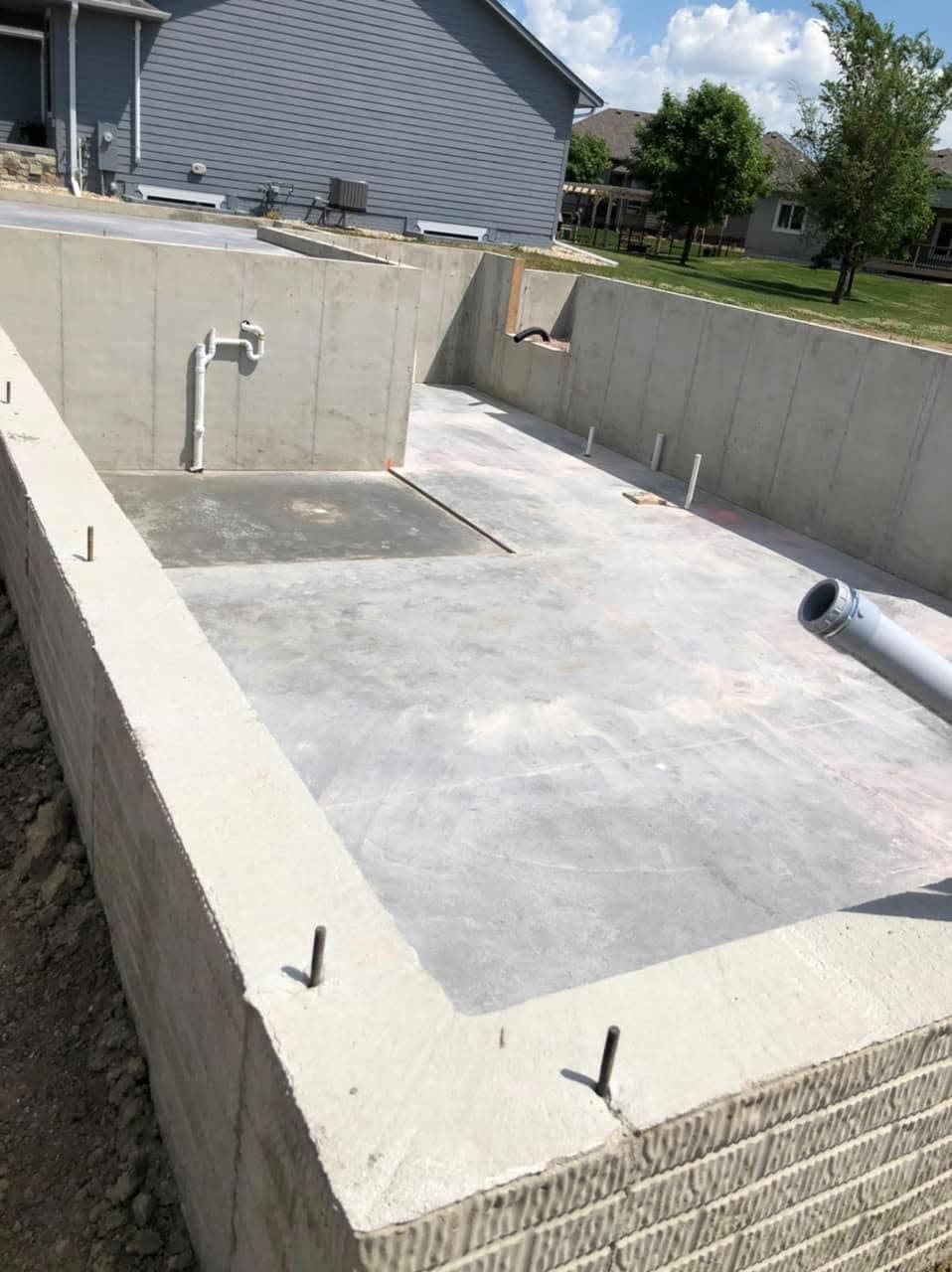 A finished basement floor slab inside poured foundation walls, with anchor bolts set along the top of the wall