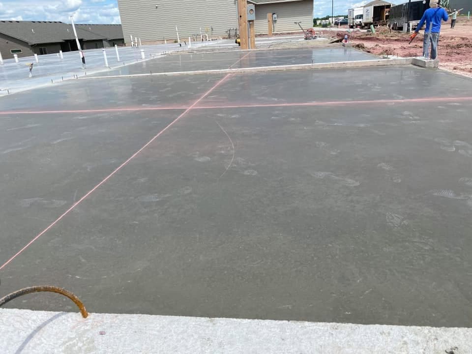 A large freshly finished structural slab with a chalk line snapped across it and a reinforcing dowel at the edge