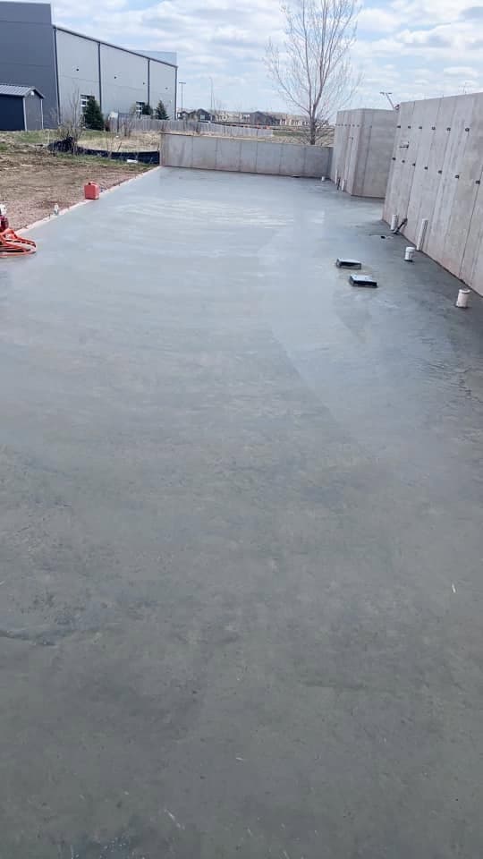 A freshly placed slab curing against a poured concrete foundation wall