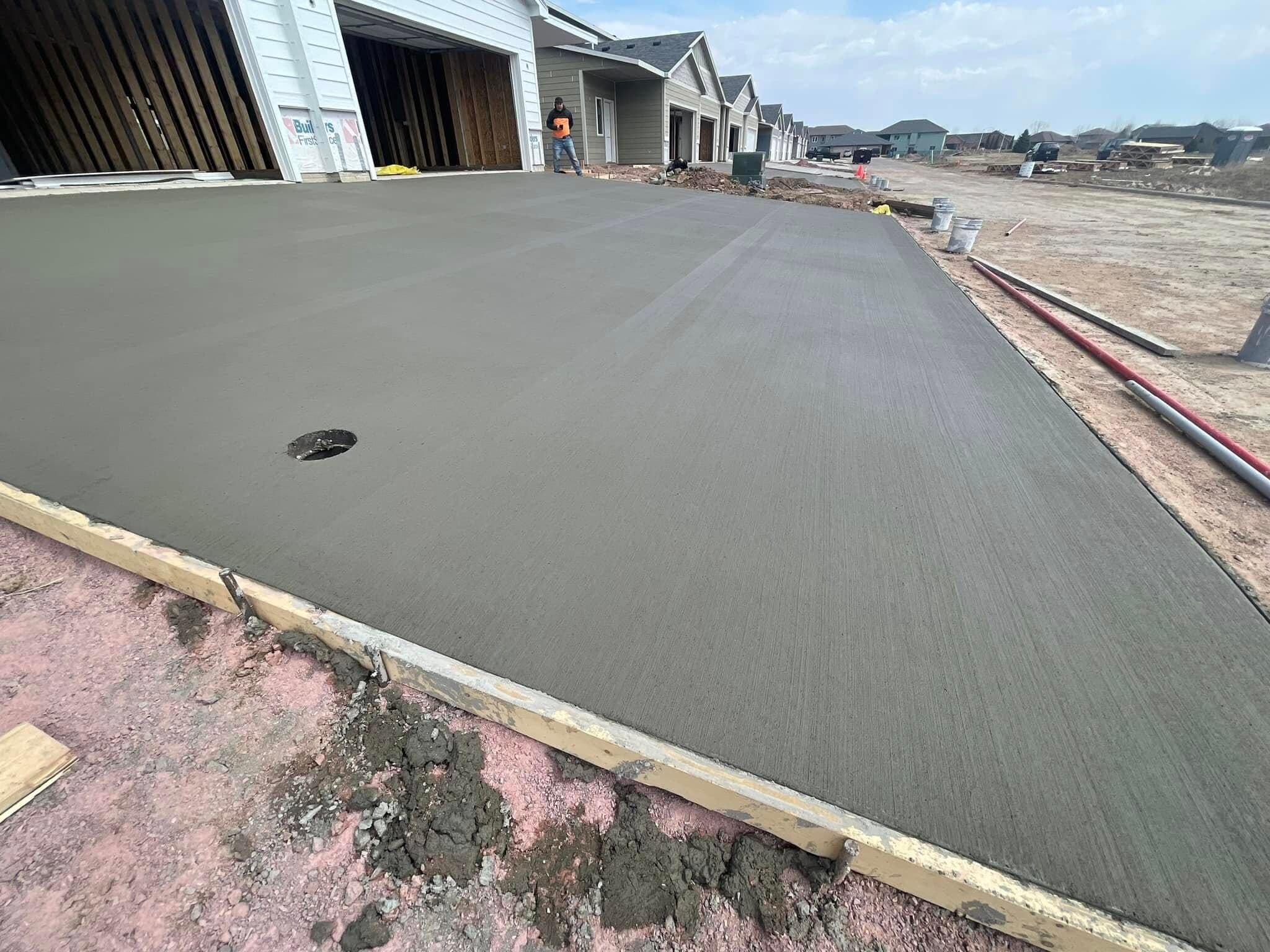 A freshly broom-finished garage slab with a center drain, poured at the open doors of a newly framed townhome garage