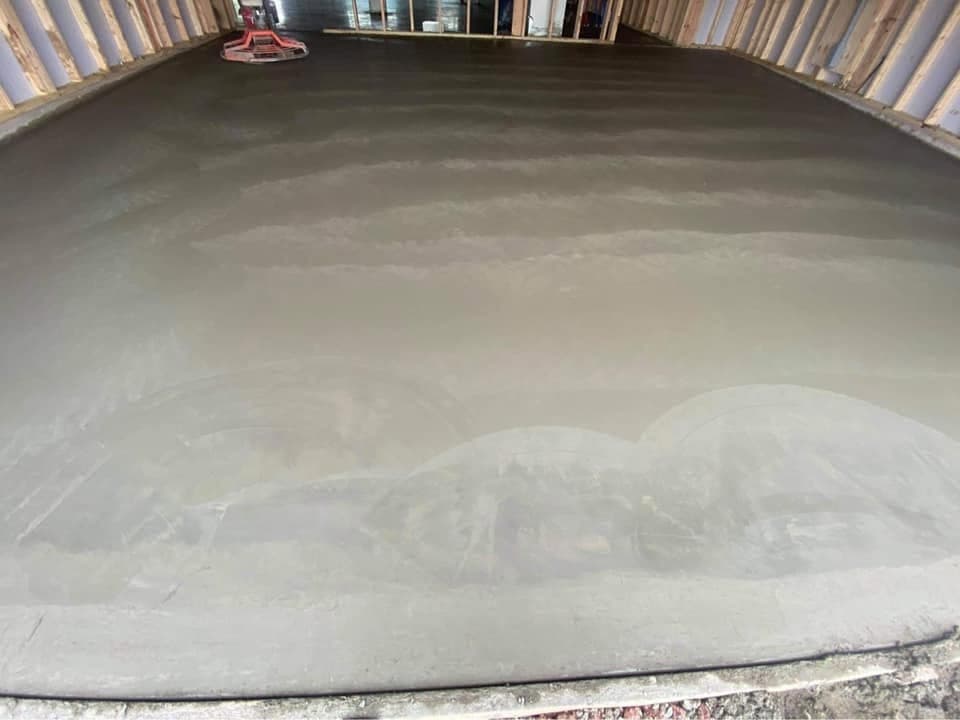 A freshly power-troweled garage floor slab inside a newly framed building, a ride-on power trowel resting at the far wall