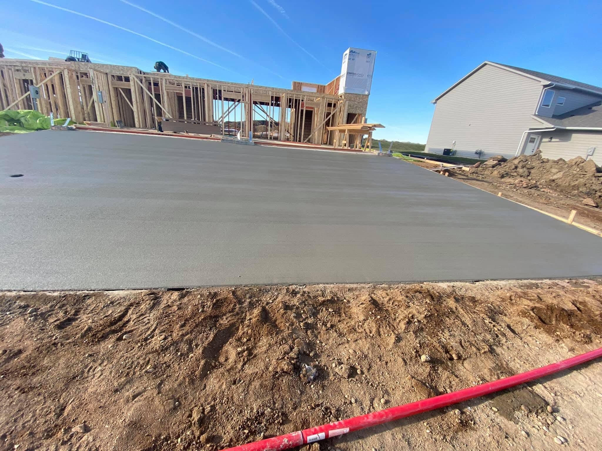 A fresh broom-finished slab of ours receding to a newly framed house