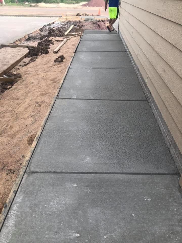 A broom-finished concrete sidewalk running along the side of a house