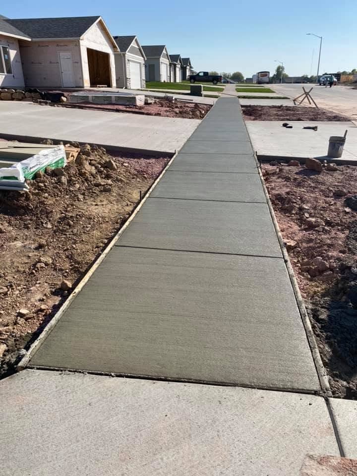 A broom-finished concrete sidewalk with cut control joints running past a row of new homes toward the street
