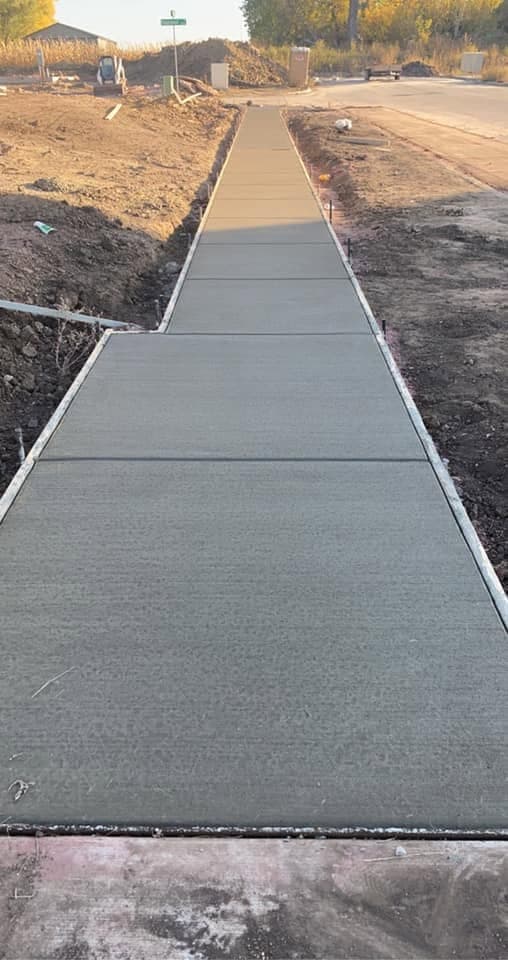 A broom-finished public sidewalk with cut control joints running alongside a new street at dusk