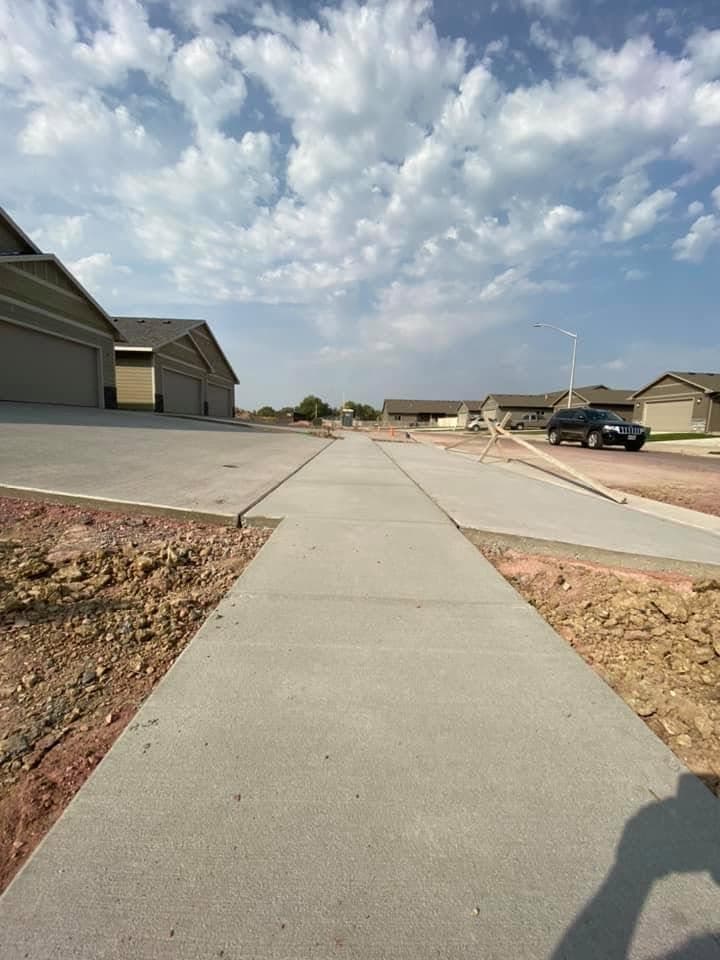 A finished, cured broom-finished sidewalk running along a residential street past a driveway approach