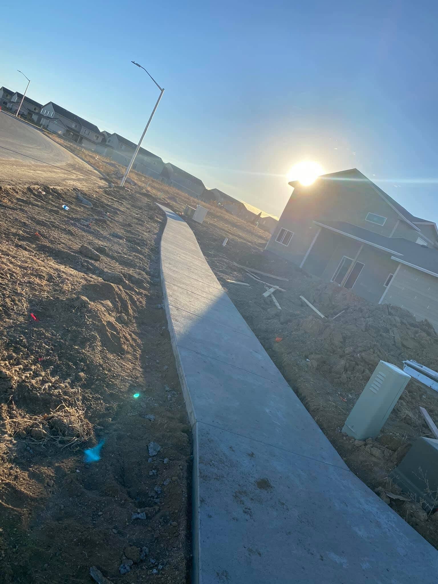 A finished broom-textured sidewalk curving through a graded lot toward a new two-story home at sunrise